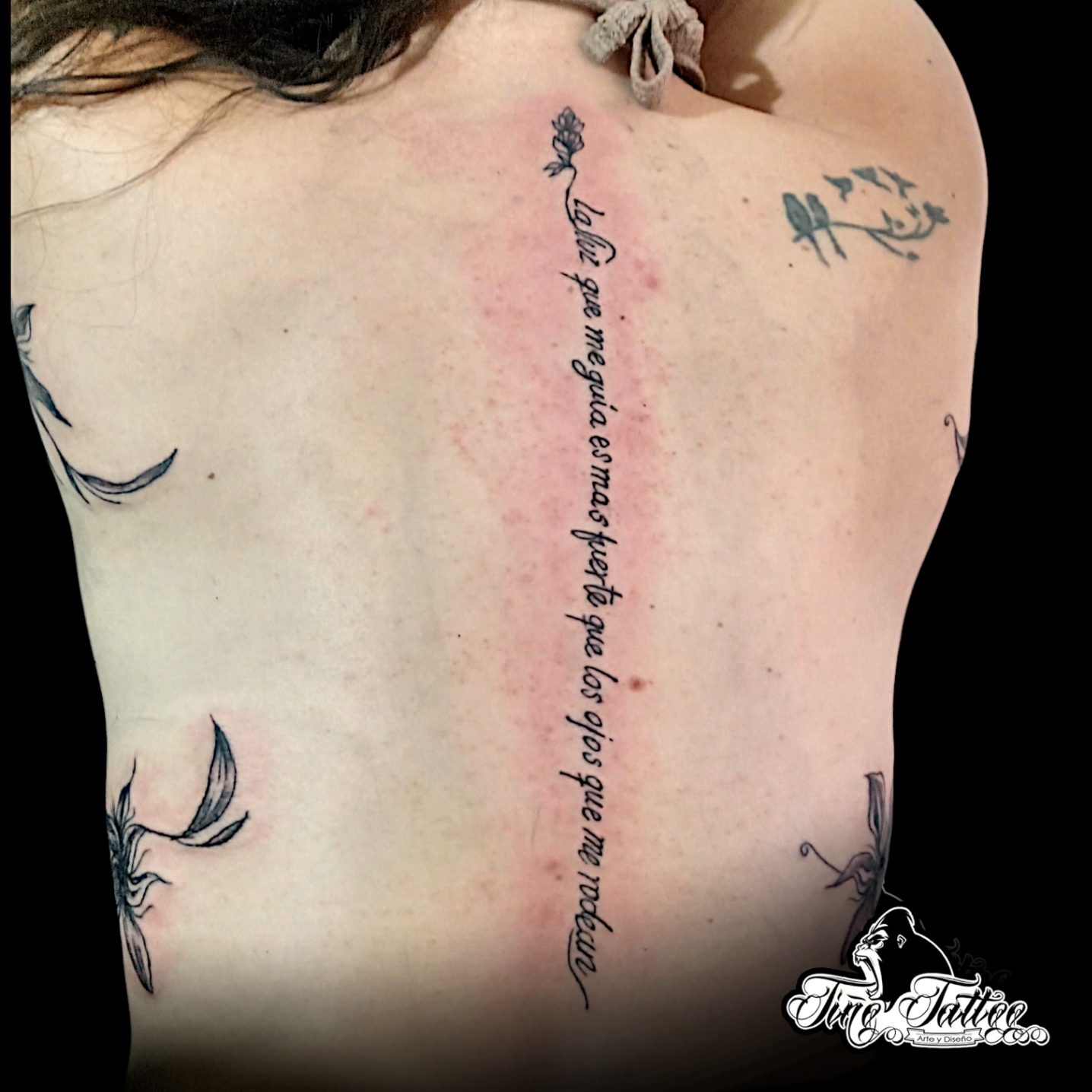 Tatuaje personalizado de frase vertical en la espalda con flor delicada en la parte superior