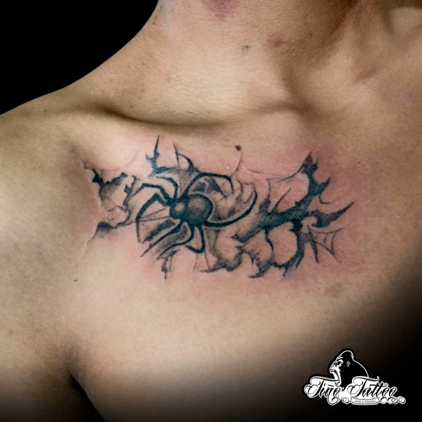 Tatuaje blackwork de araña con efecto rasgado y telarañas sobre la clavícula