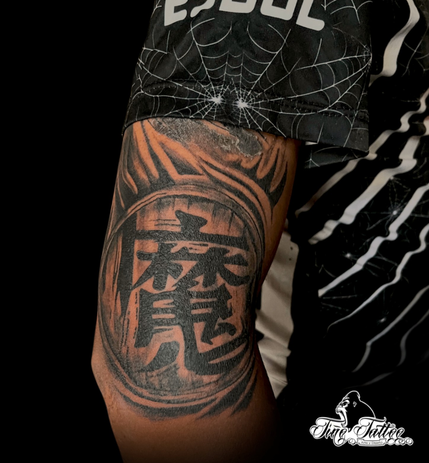 Tatuaje blackwork con gran kanji central y fondo en tonos cálidos sobre el brazo