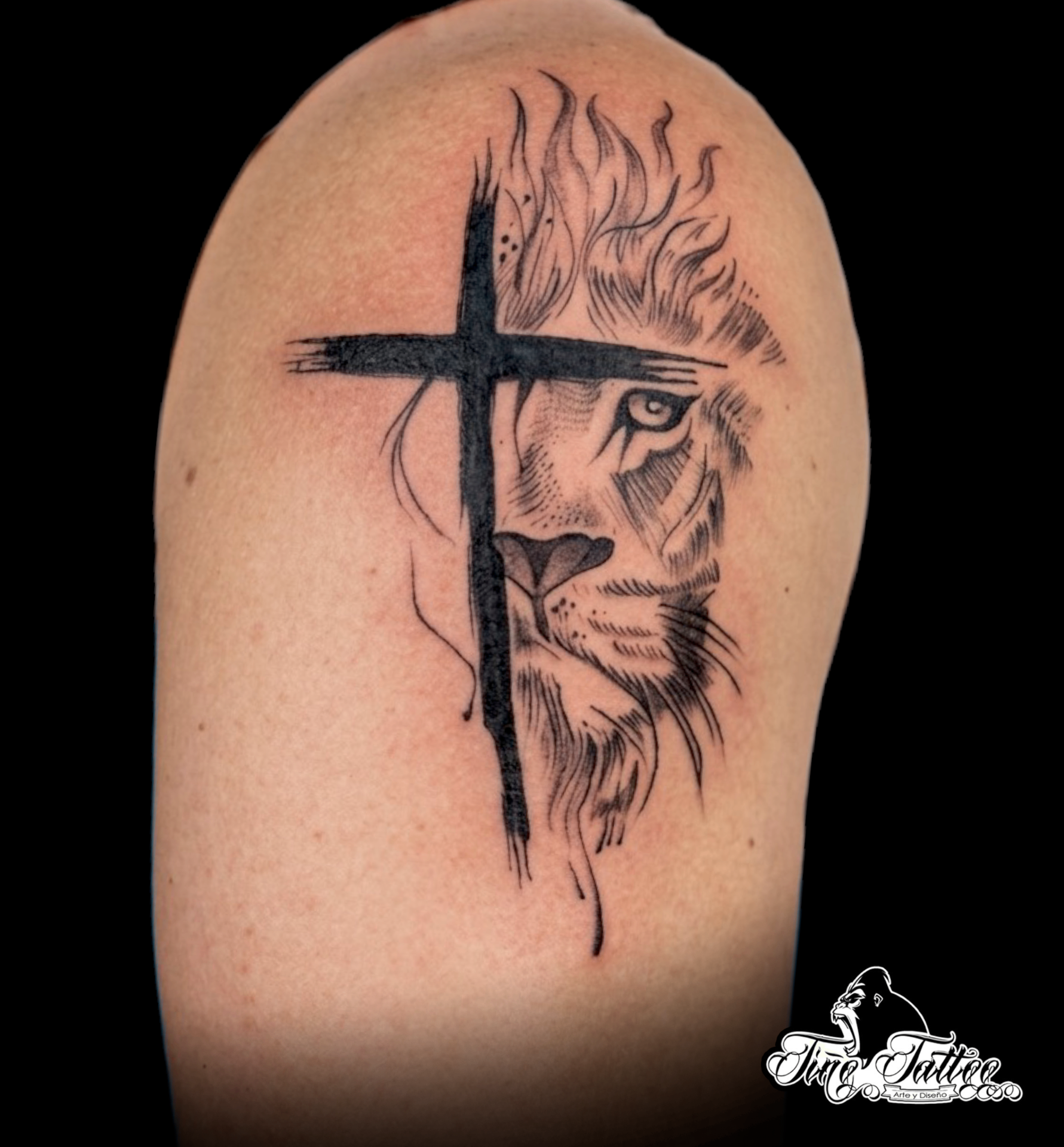 Tatuaje blackwork de cruz negra superpuesta con medio rostro de león en el hombro