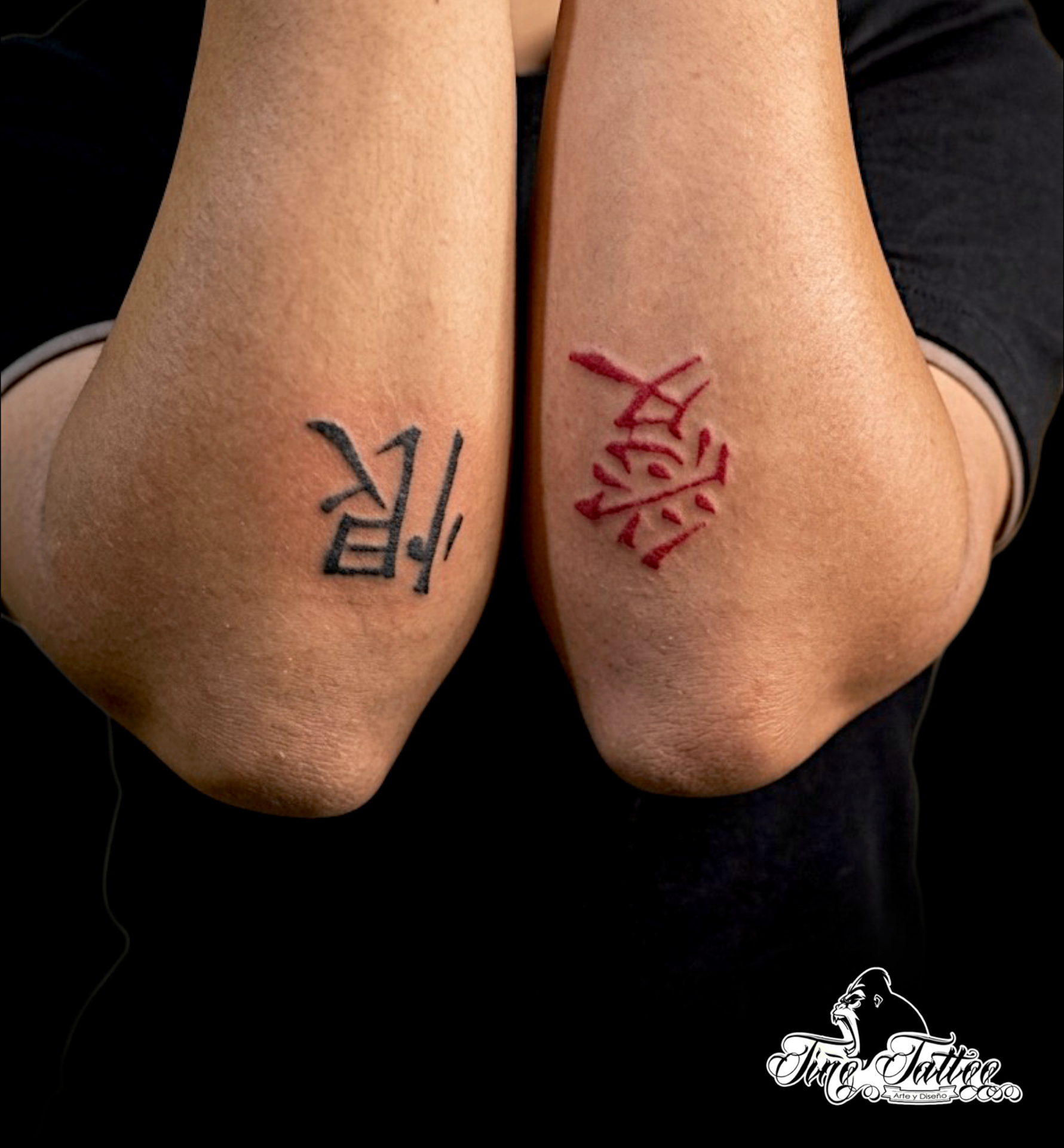 Tatuajes a juego de símbolos estilo kanji en codos, uno en negro y otro en rojo