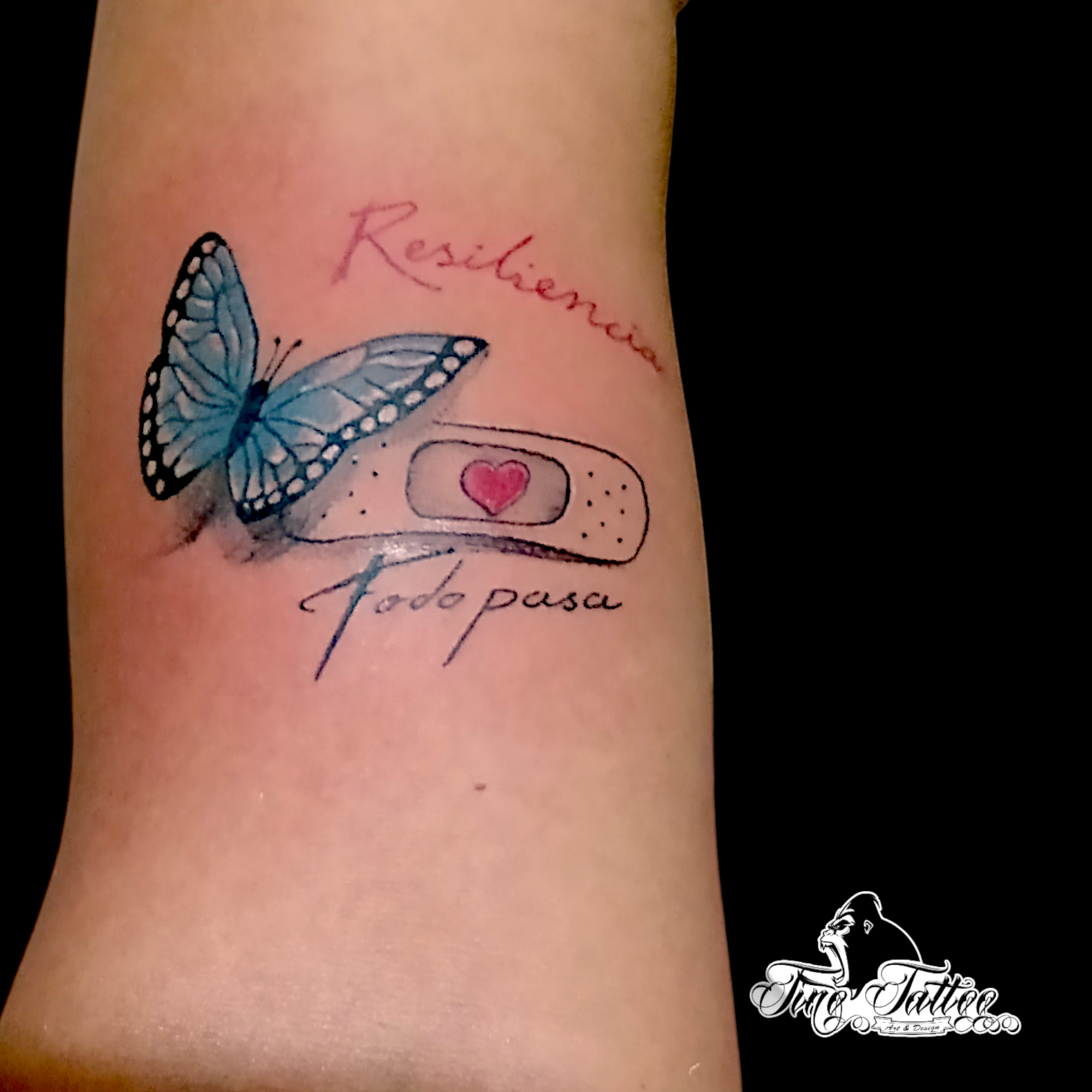 Tatuaje de mariposa azul con curita y lettering de resiliencia